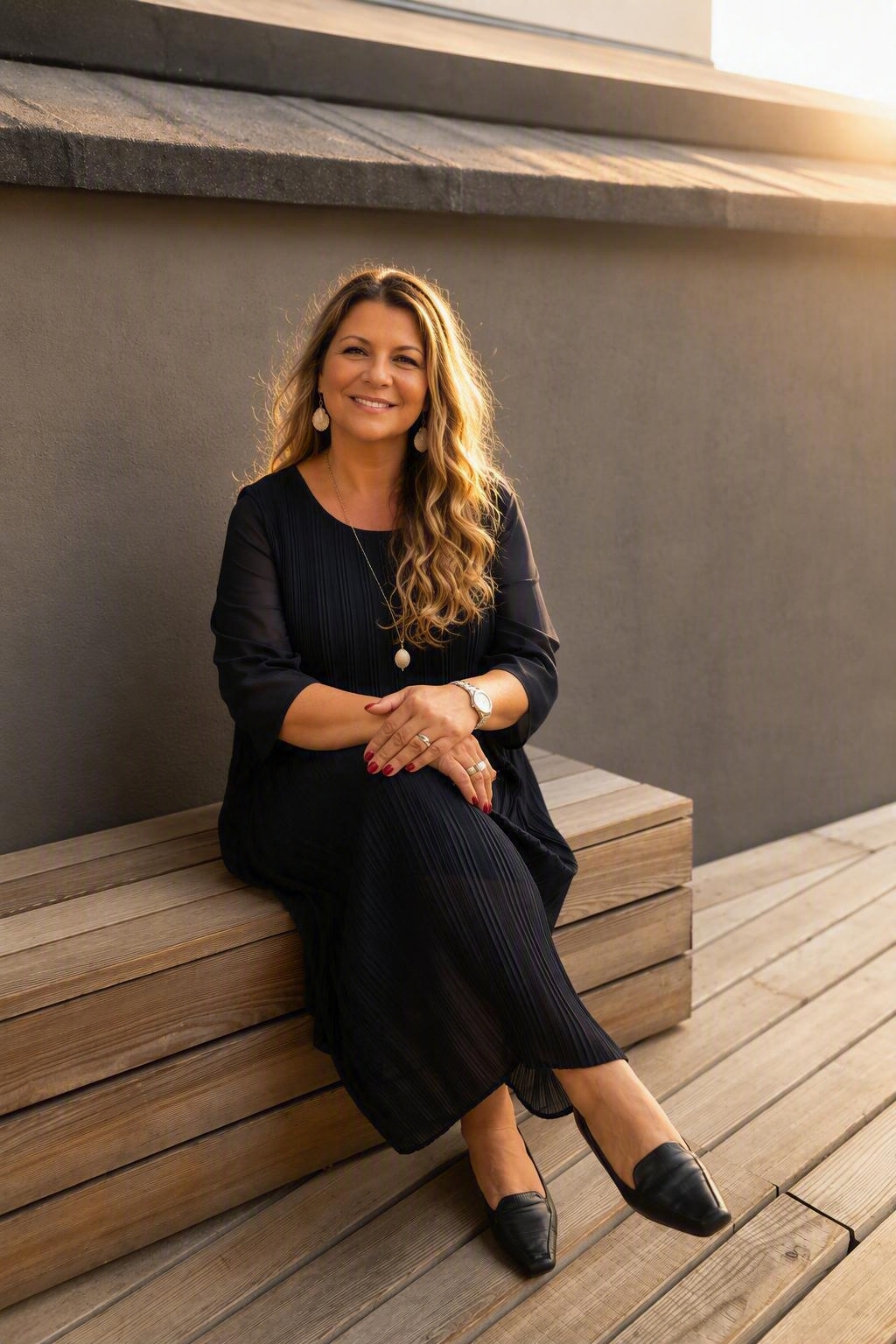 Christiane Vogel sitzt auf einer Bank vor einer ruhigen grauen Wand.